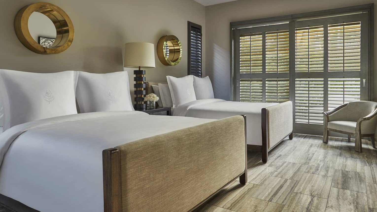Two double beds in a serene guest room with wood floors, neutral tones and large shuttered windows