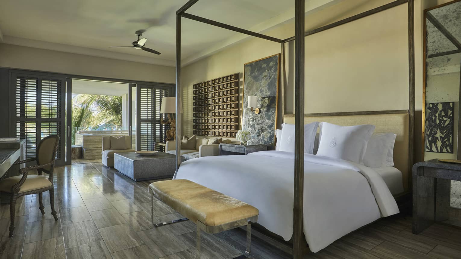 Spacious bedroom with a canopy bed, soft neutral décor, a bench at the foot and large windows overlooking a tropical garden