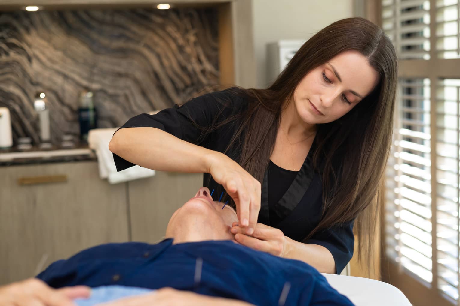 Woman performs acupuncture on person's face at luxury resort spa