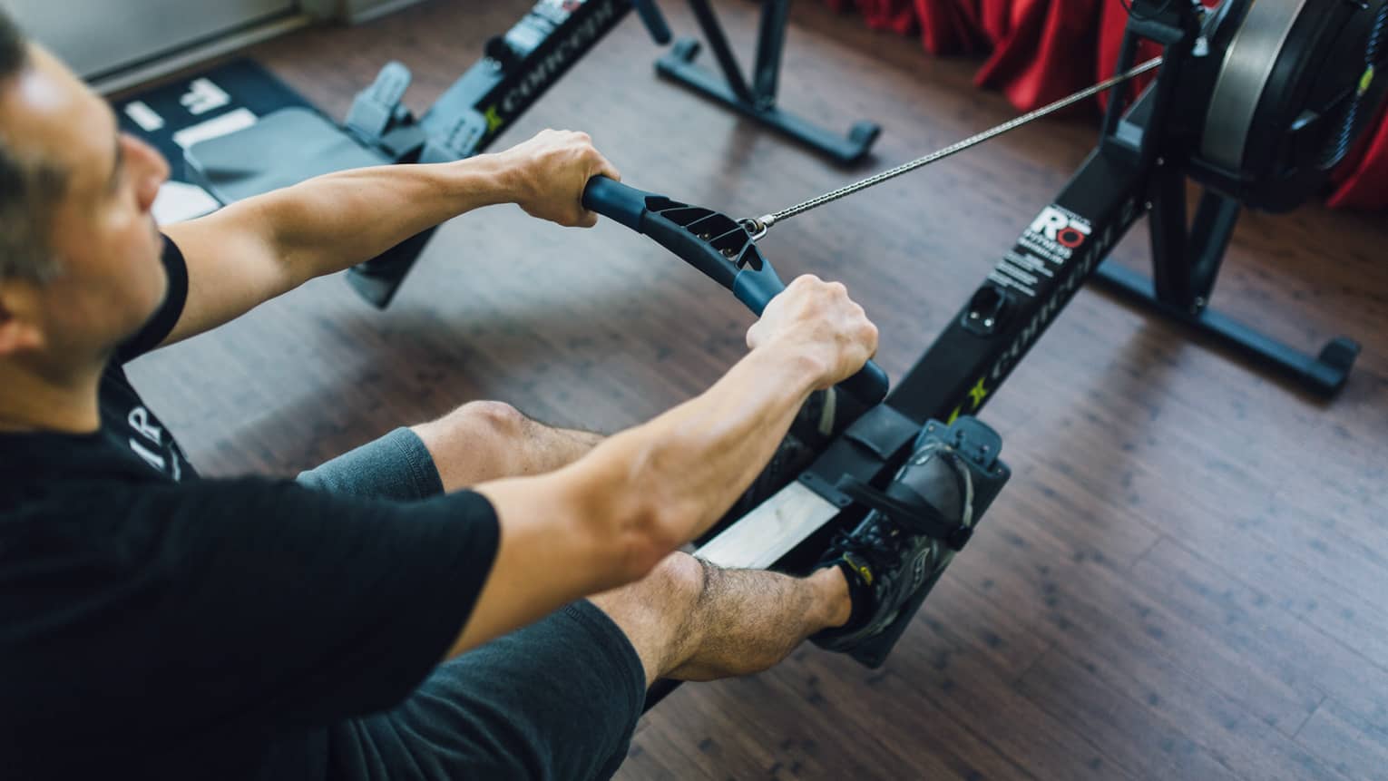 Man sits, pulls handle of cardio rowing machine in fitness facility 
