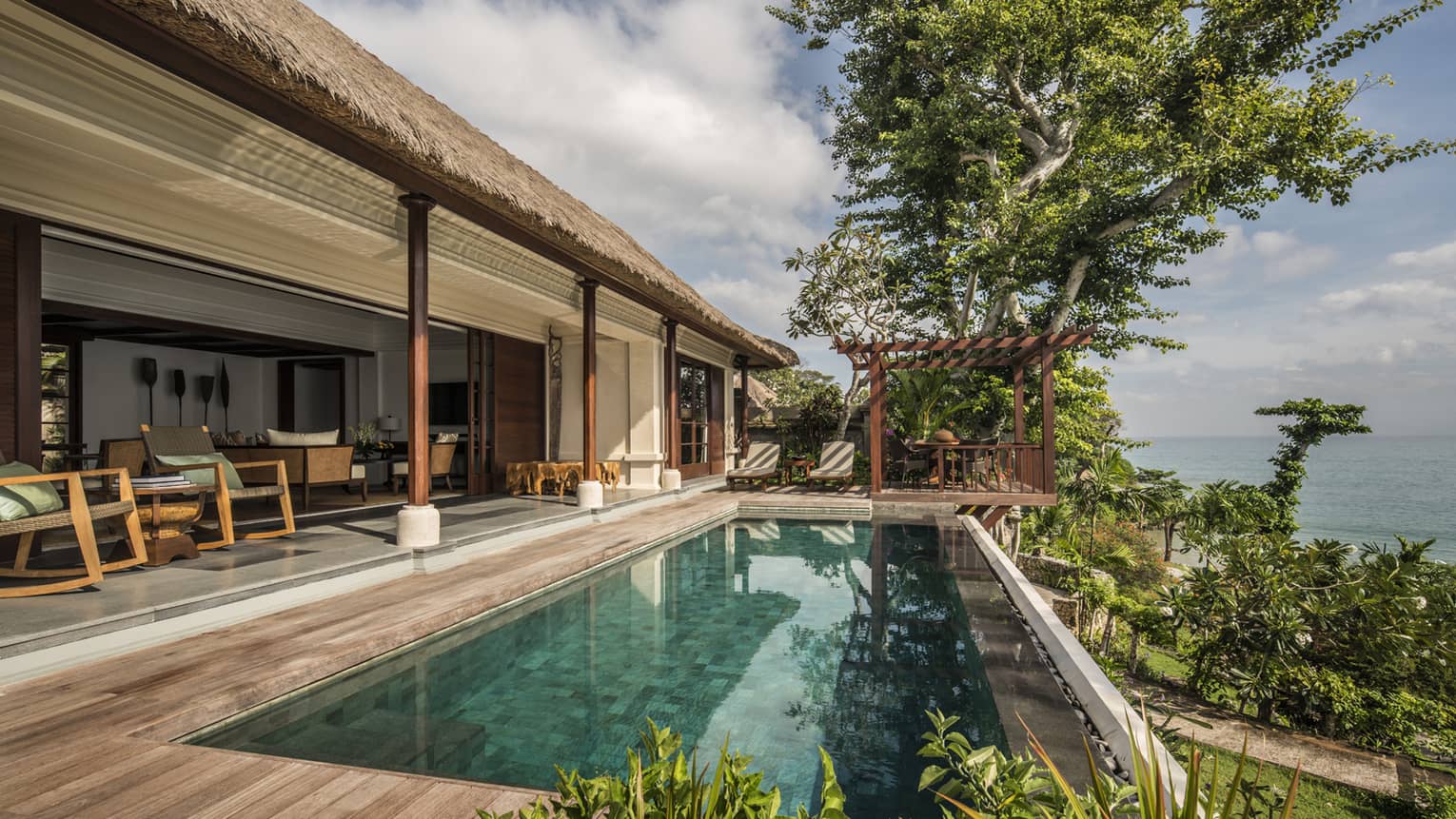 Villa patio with rectangular swimming pool, thatched roof over shaded seating area