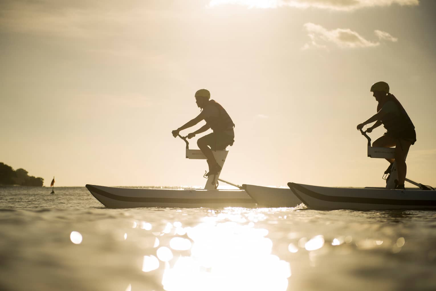 Silhouettes of two men riding aquatic bicycles on ocean at sunset