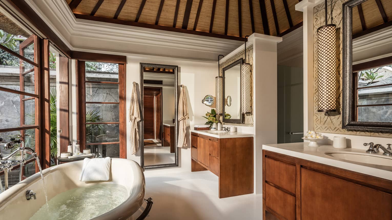 Water runs from faucet into deep tub in Imperial Villa bathroom with double wood vanities, mirror