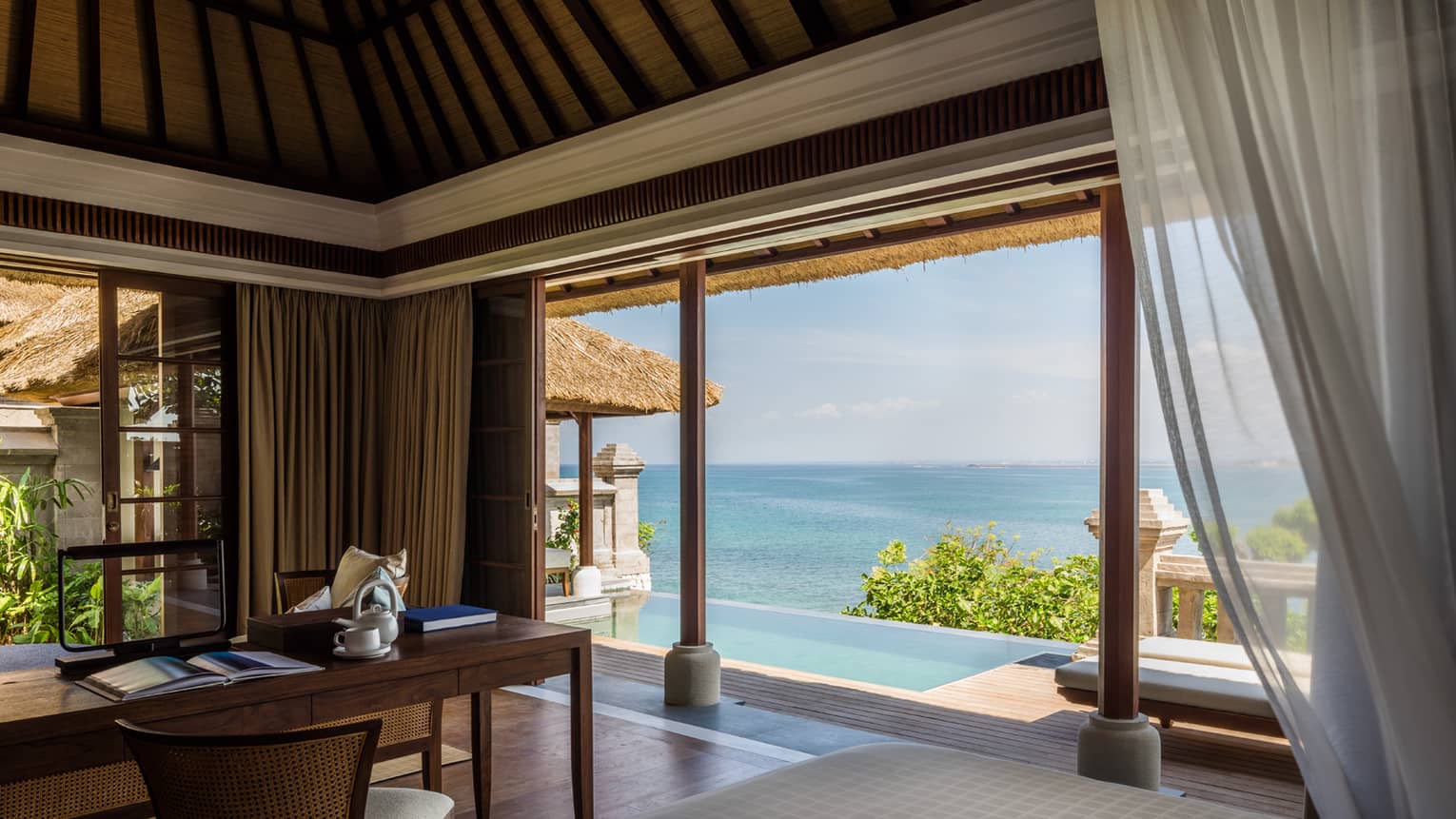 Wood writing desk with open book, coffee mug, open wall to patio and infinity pool, ocean view