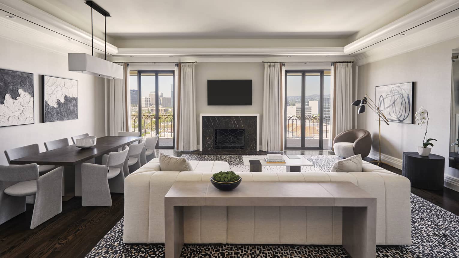 Living area with white sofa, artwork, TV, fireplace and dining table with 8 modern grey chairs
