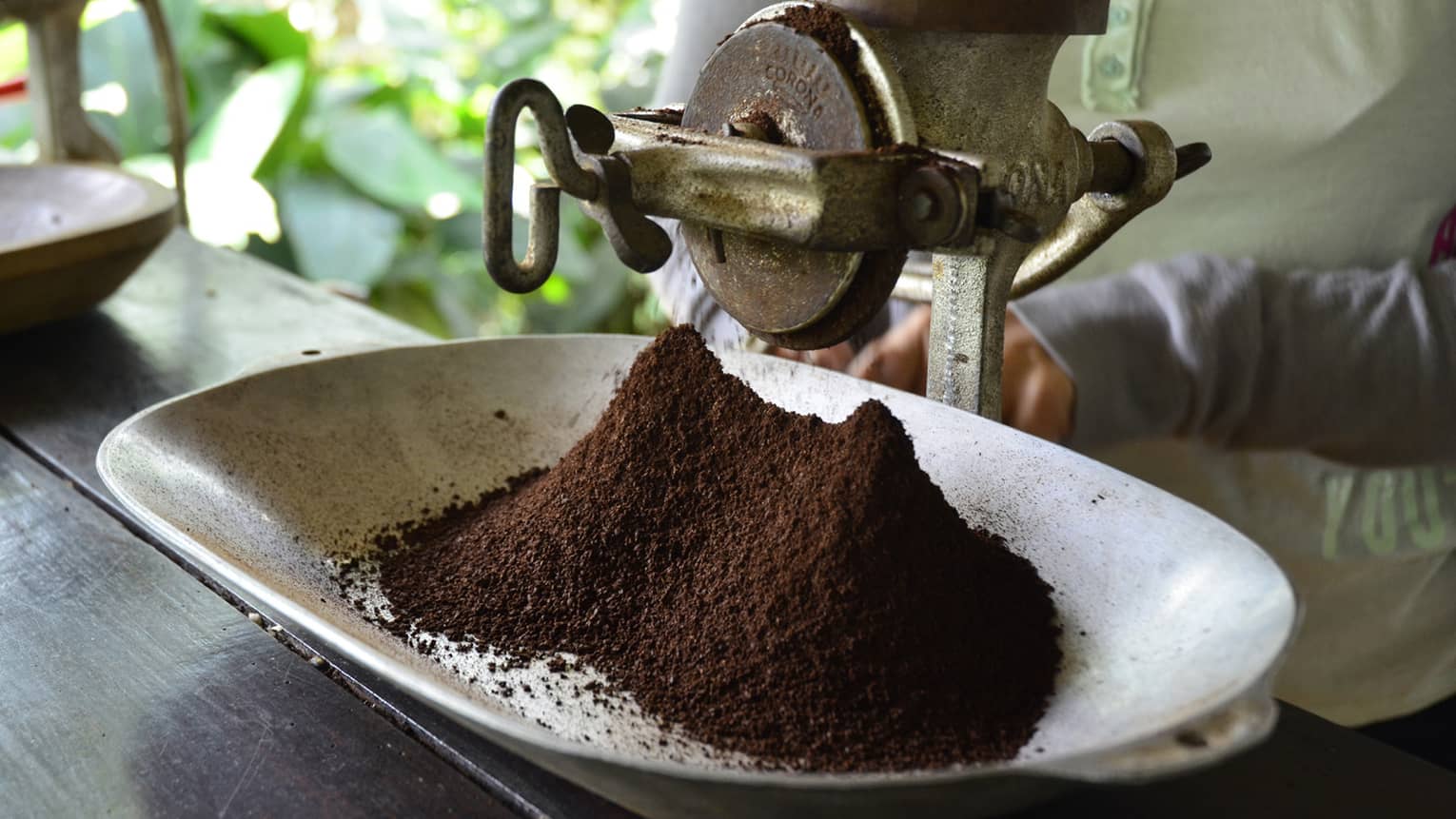 Large metal industrial-looking hand grinder with pile of ground Colombian coffee