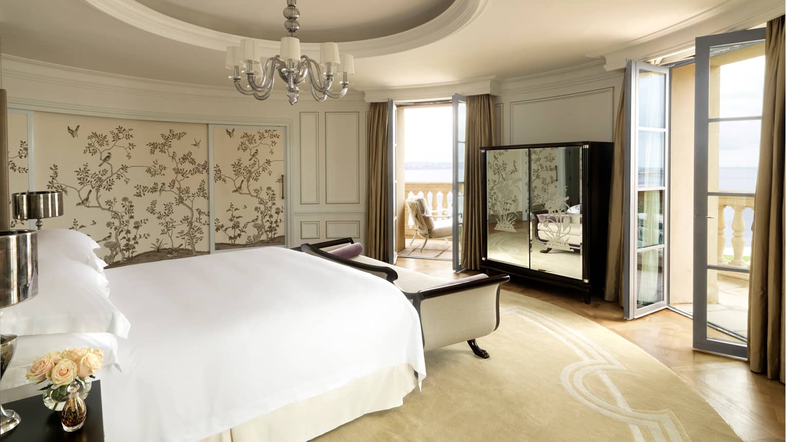Round hotel room with recessed dome in ceiling, small chandelier, bed with white chaise, mirrored dresser, two patio doors