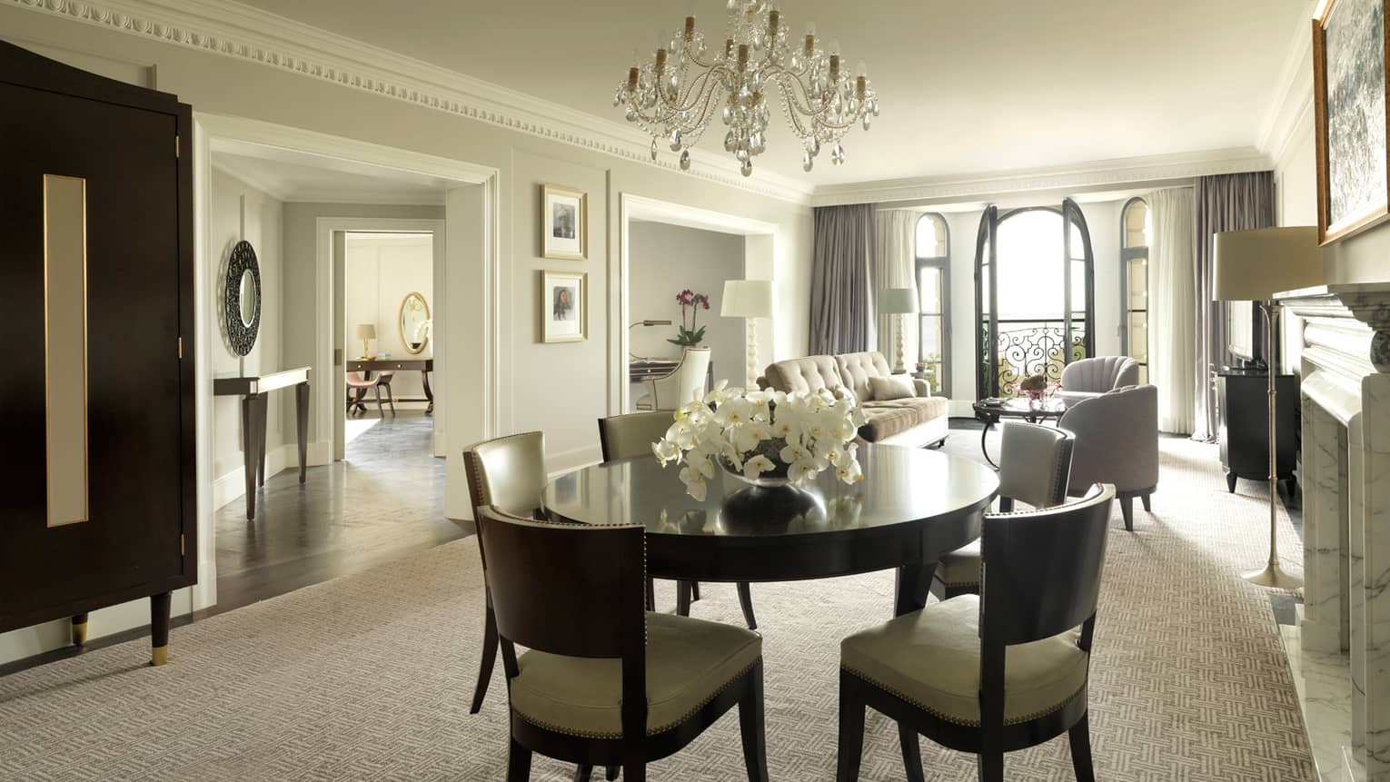 One-bedroom Suite round dining room table for 6, small crystal chandelier, living room, French doors to balcony in background