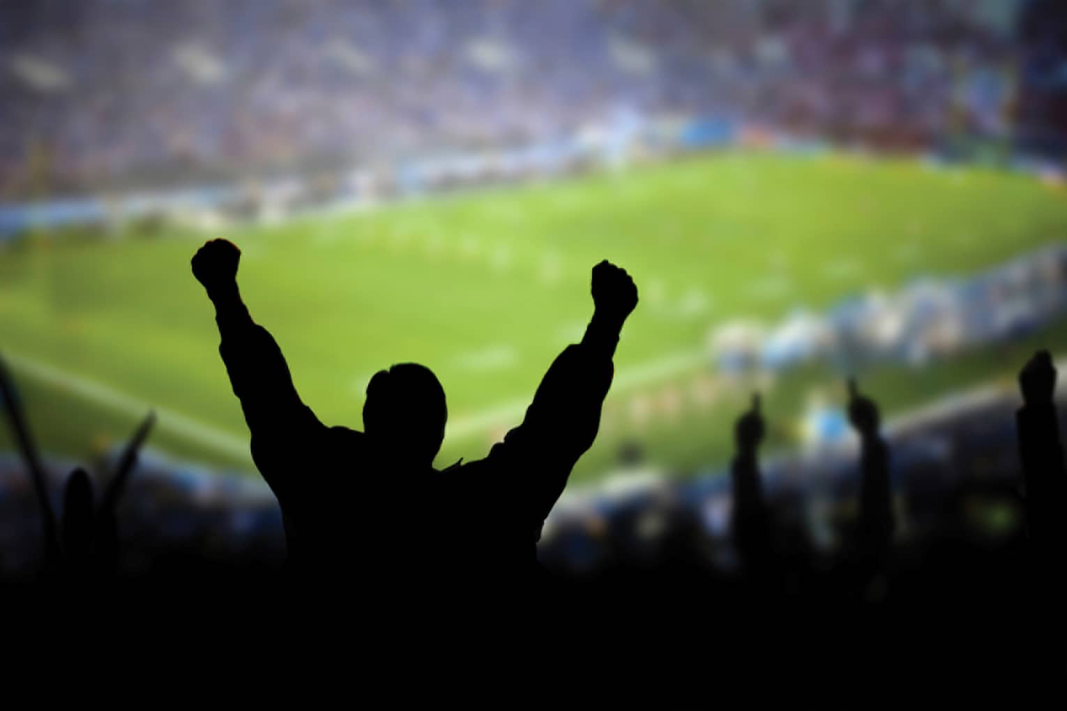 A silhouette of a person cheering at a football stadium.
