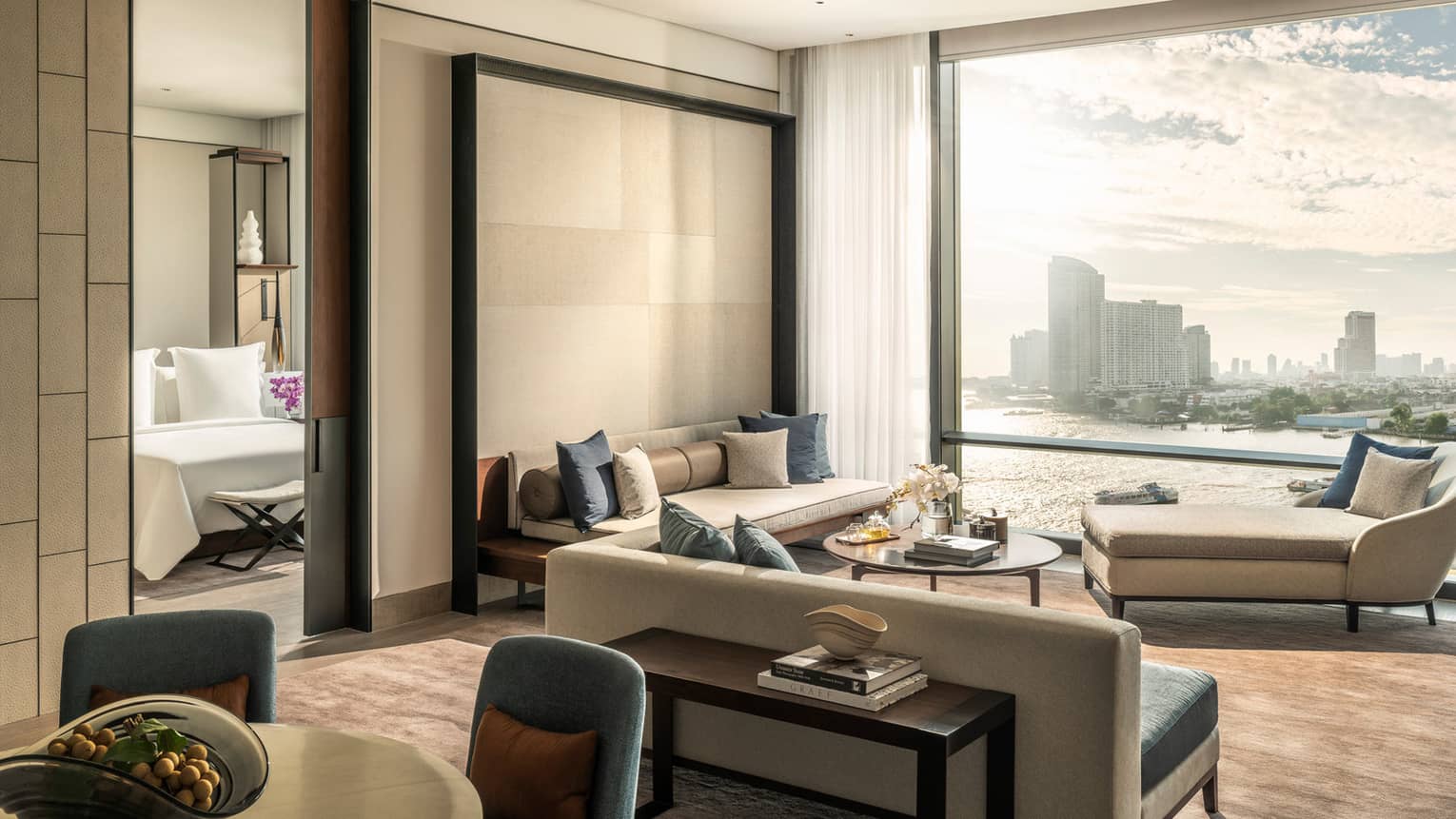 Hotel suite's living area with two sofas, chais lounge, wall of windows, connecting to bedroom