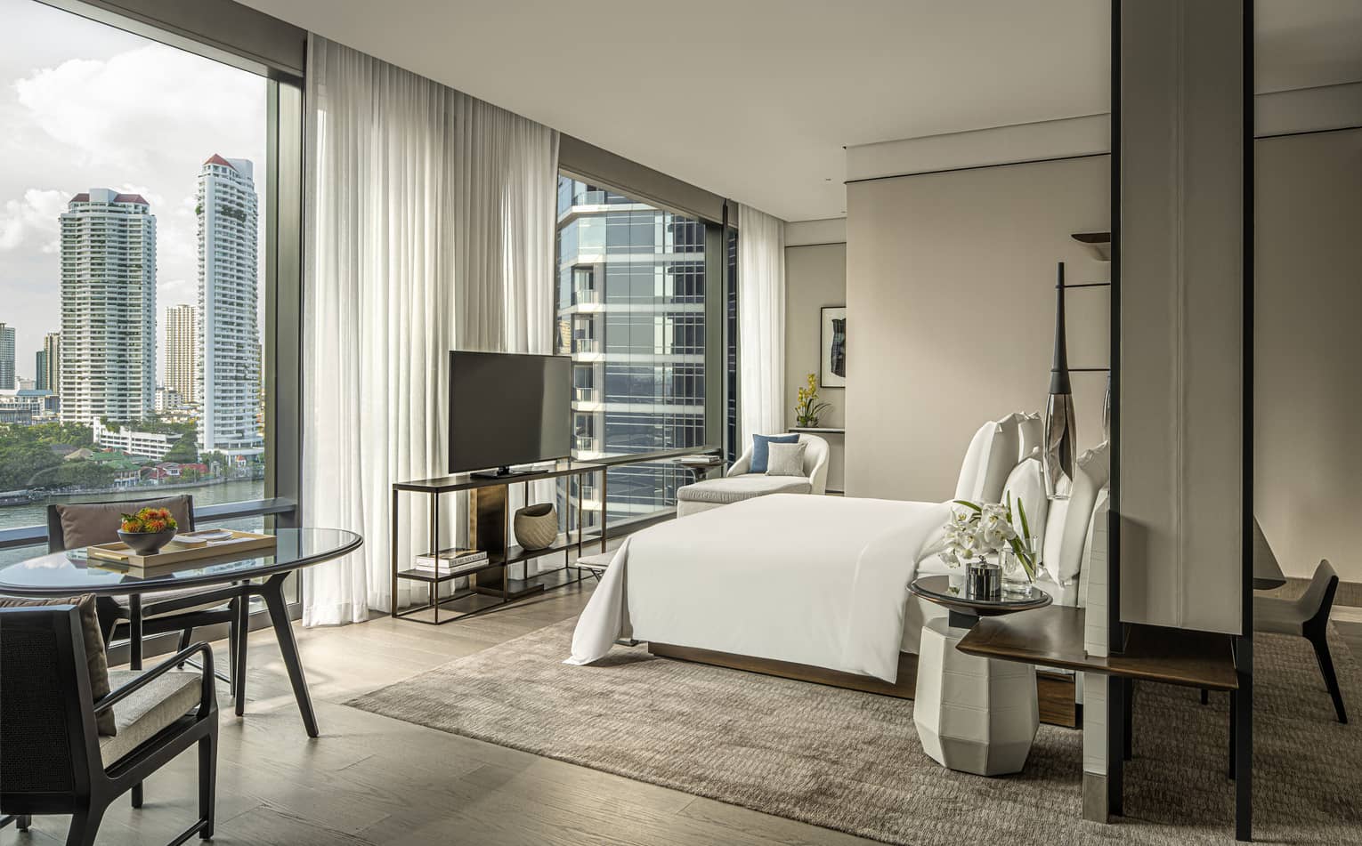 Hotel room with king bed, table and two chairs, TV and wall of windows