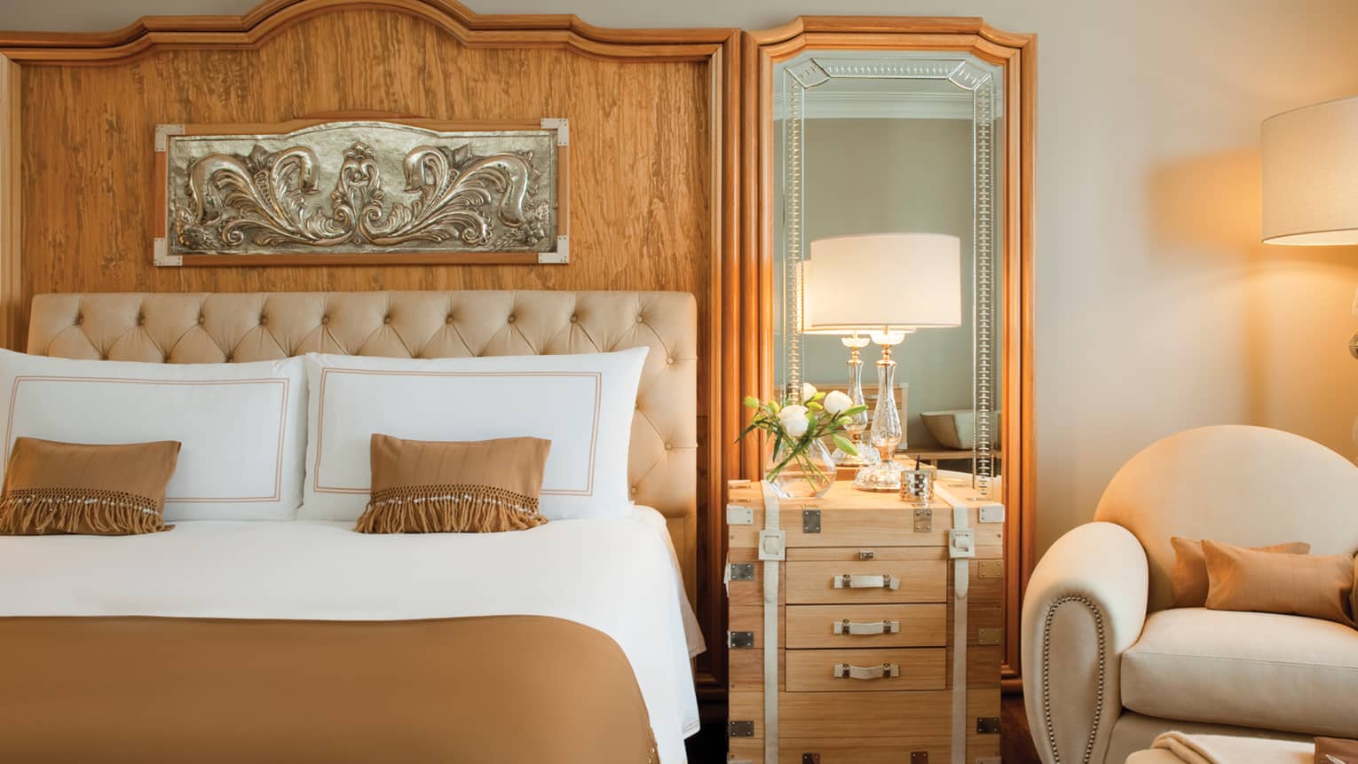 Close-up of hotel room bed with brown bedspread, accent pillows with tassels, wood headboard with silver art 