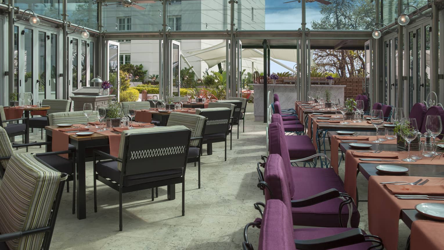 Nuestro Secreto outdoor dining room in glass patio with purple chairs, orange linens on table