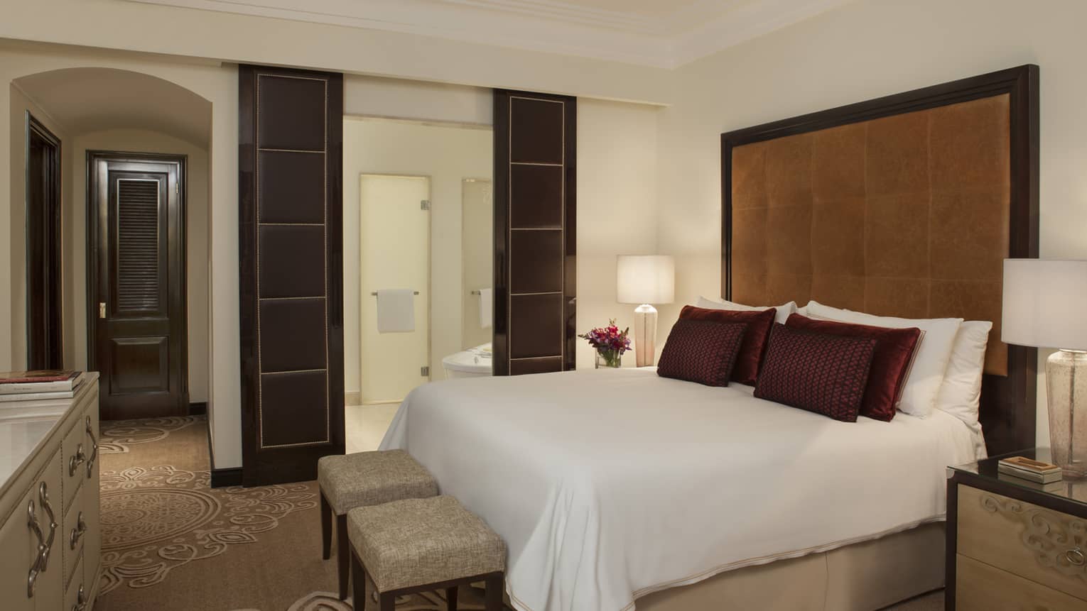 E-Lounge One Bedroom Suite bed with tall padded brown headboard, leather wall panels, two small benches 