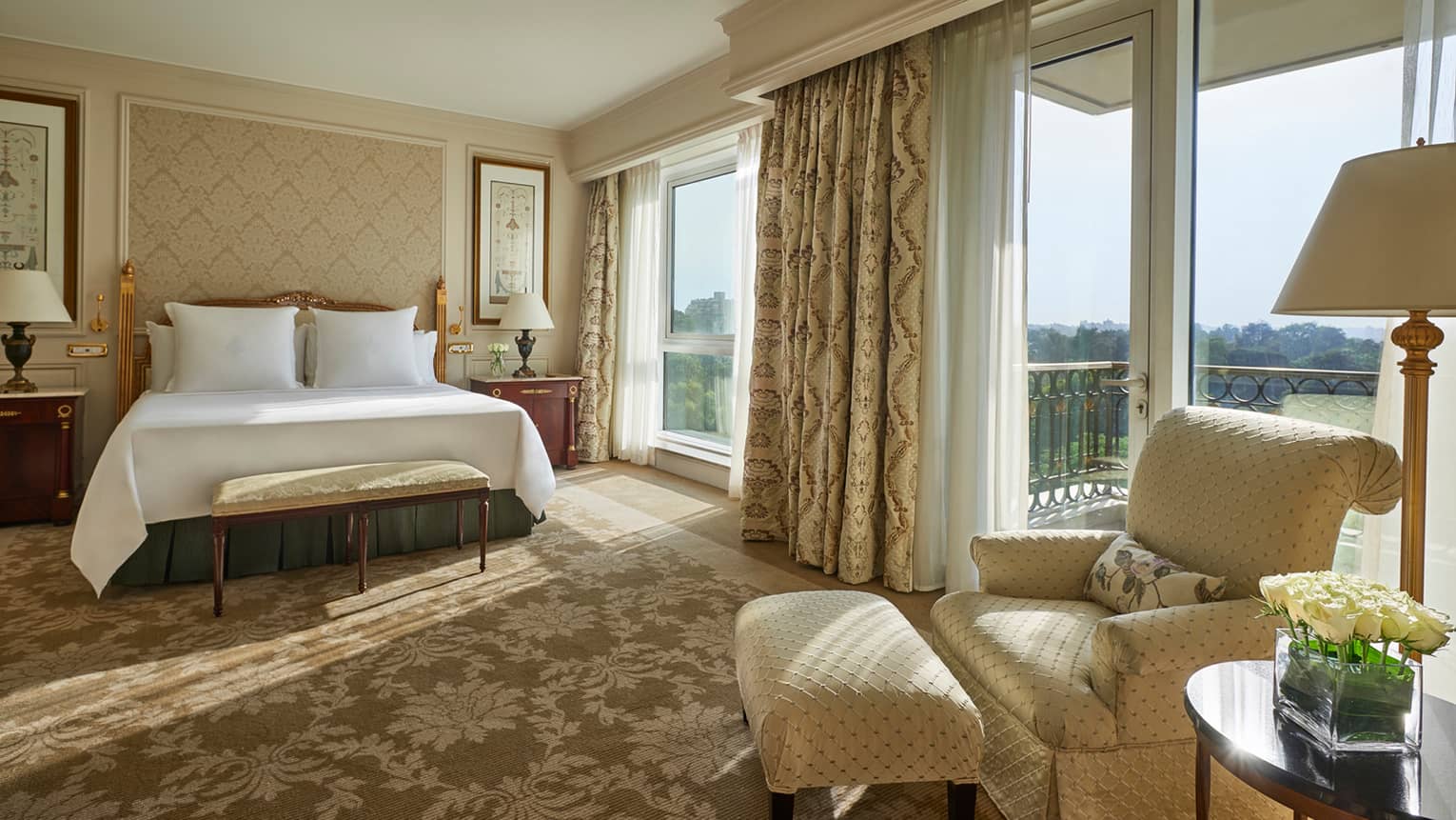 Deluxe Room bed, cream-coloured armchair beside sunny floor-to-ceiling patio door and window
