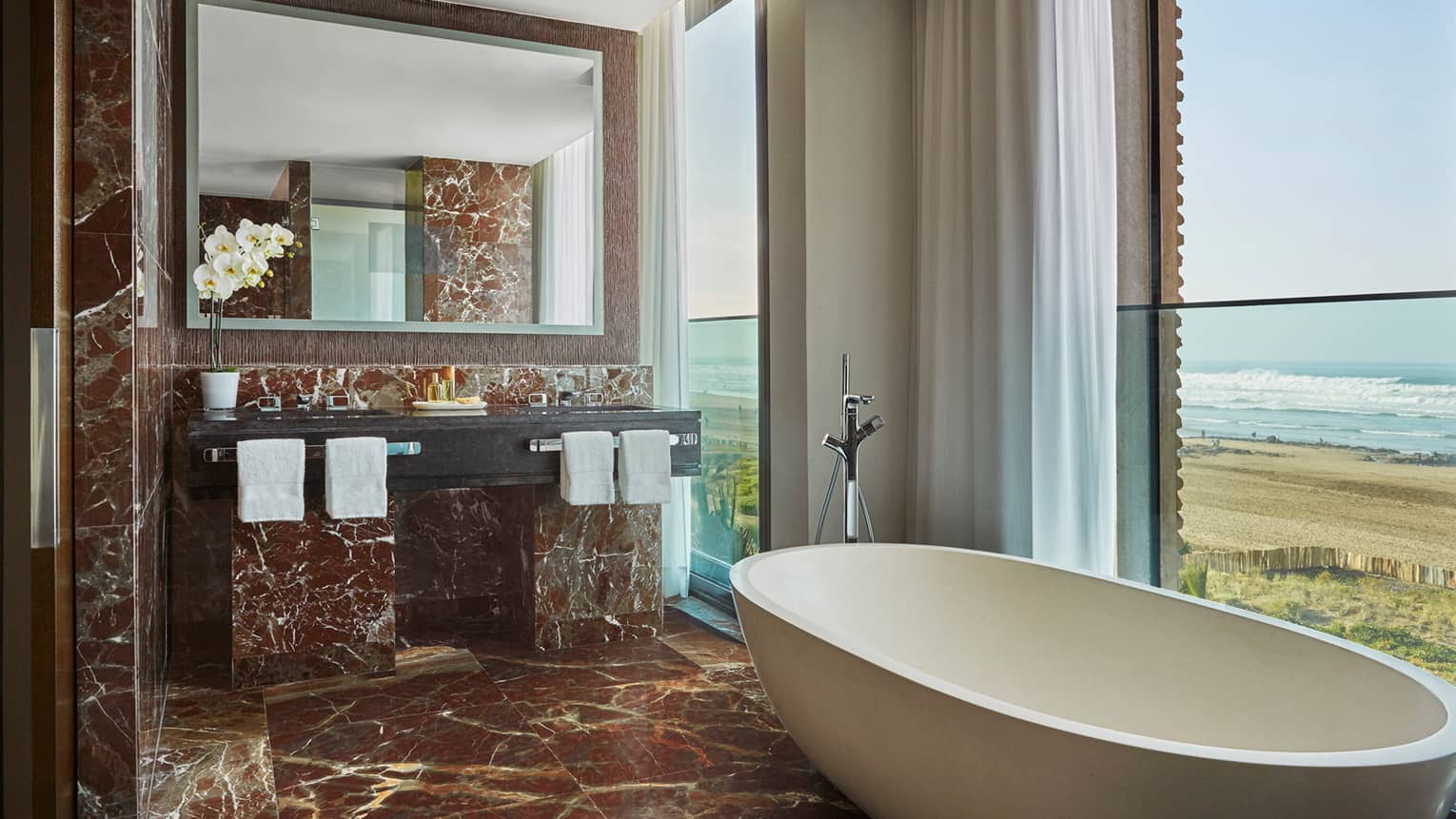 Signature Suite bathroom with deep soaker tub in front of window with ocean view, brown marble floor, wall