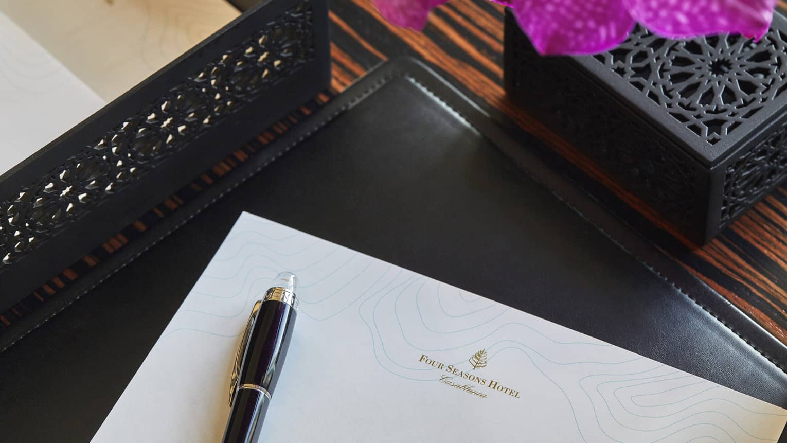 Corner of white piece of paper with Four Seasons logo, pen