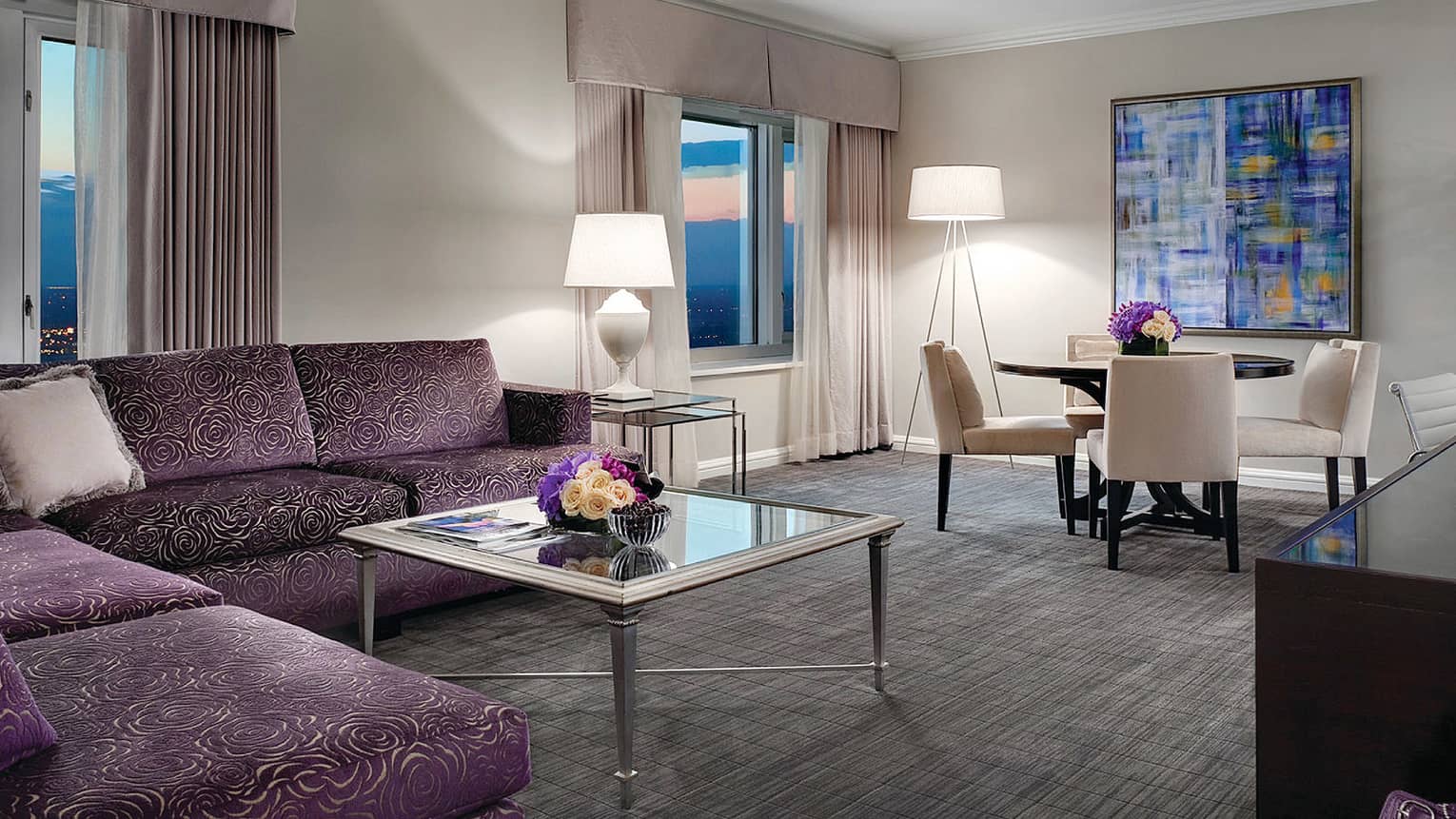 Suite with large L-shaped purple velvet sofa with rose pattern, glass table with fresh roses, four-seat dining table