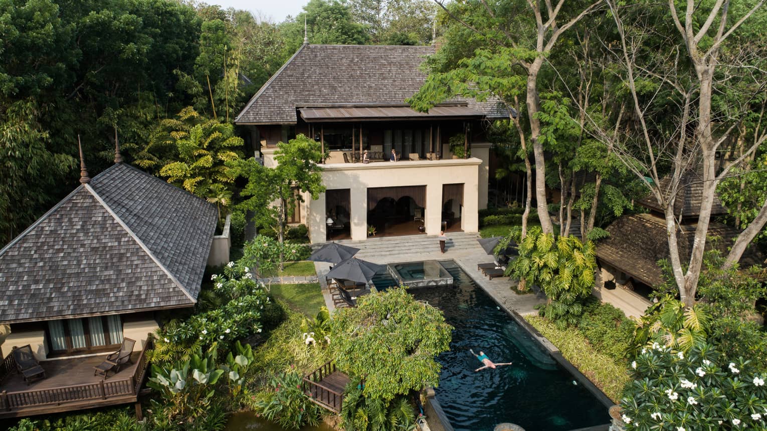 View over large villa exterior, outdoor swimming pool where man floats in water 