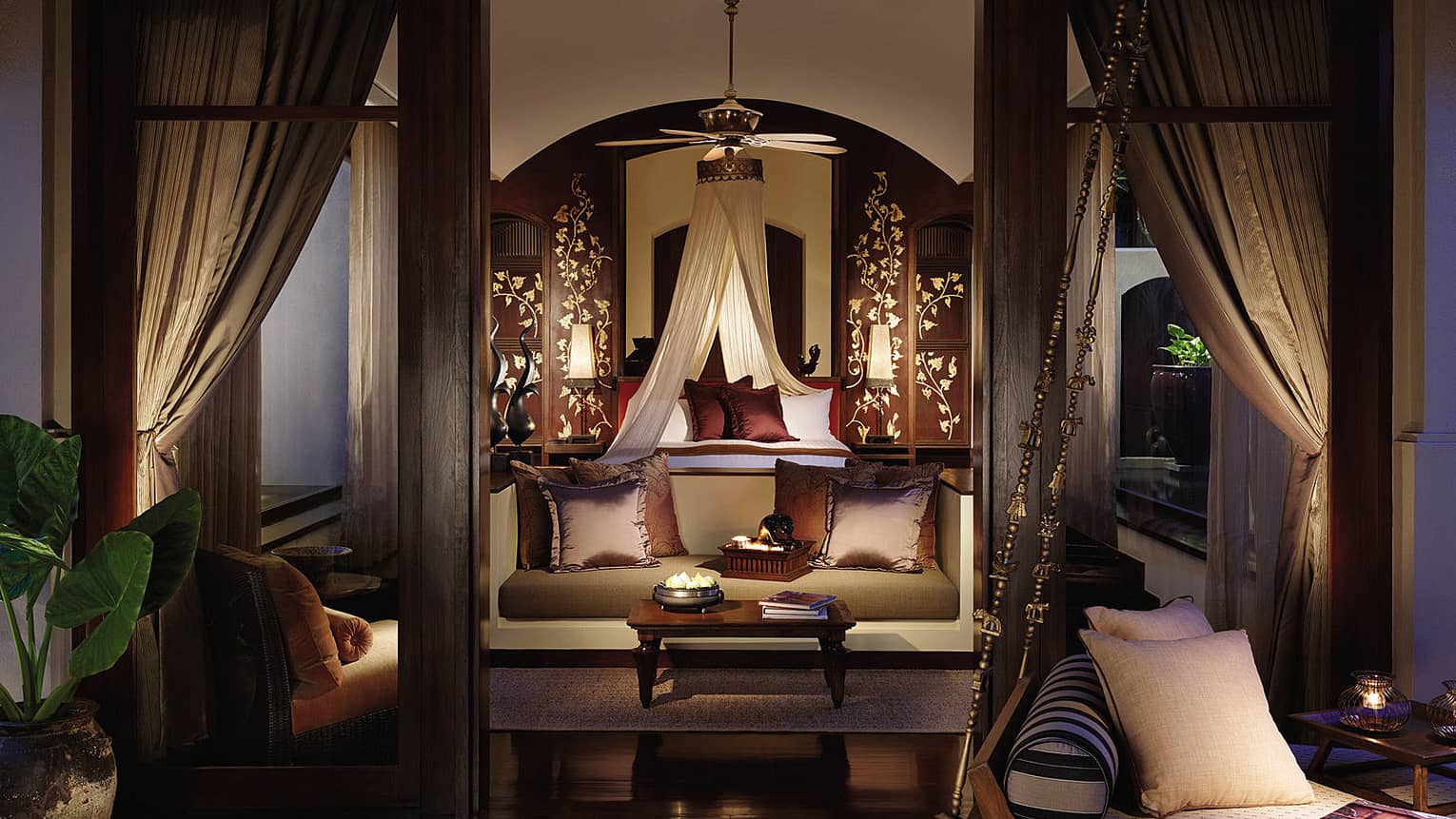 View from doorway into elegant Pool Villa with loveseat and brown silk pillows, white canopy over bed