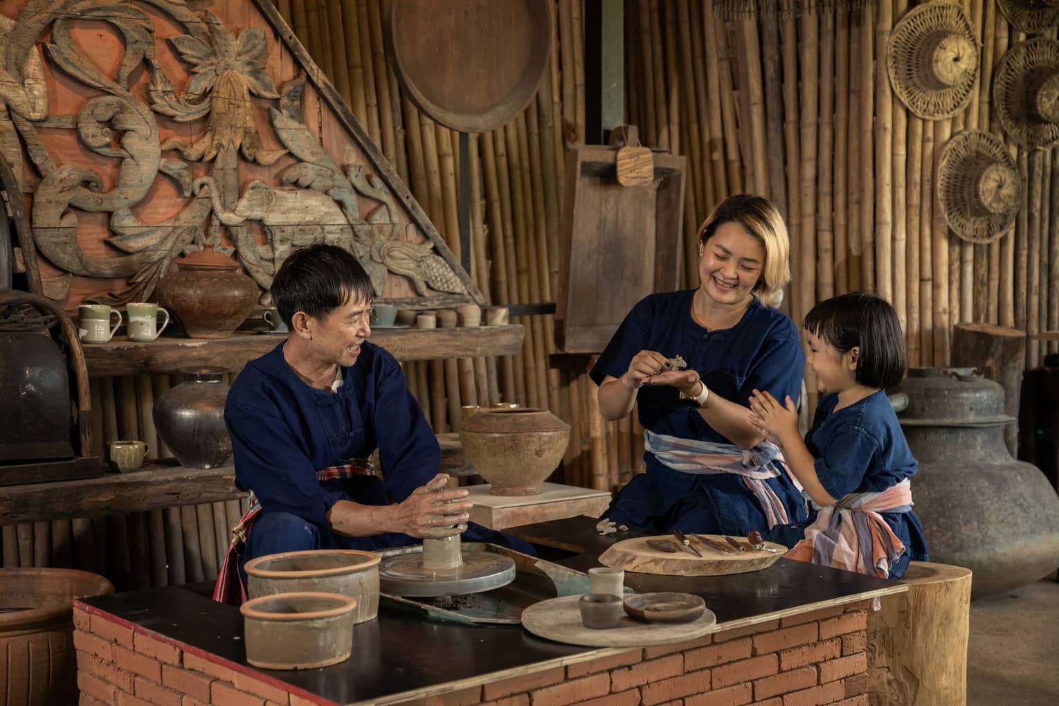 A potter teaching a woman and a child to shape clay in a rustic pottery workshop, surrounded by traditional tools and pottery.