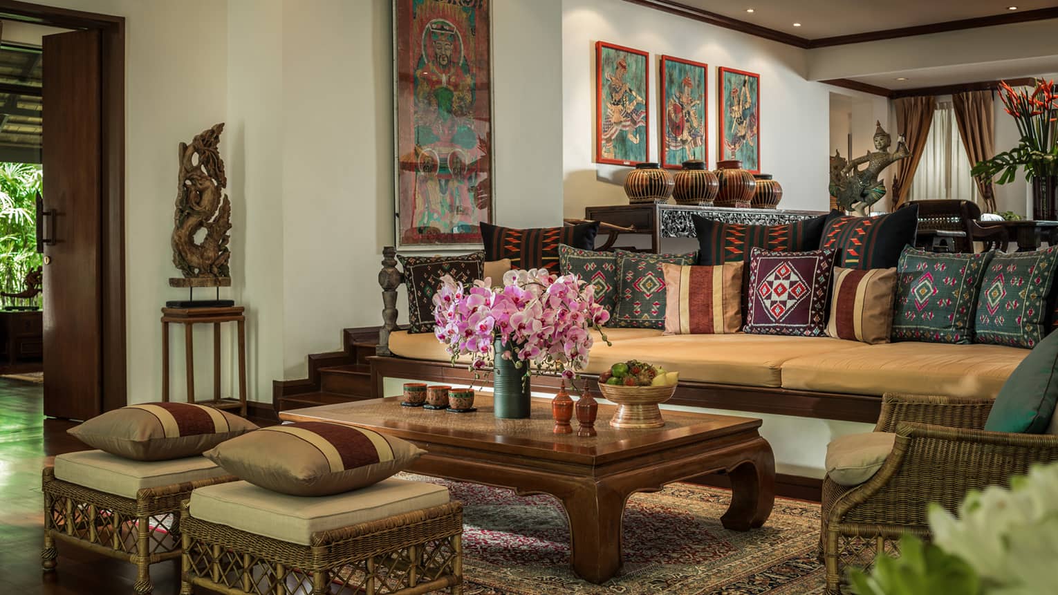 Residence living room with long sofa and two ottomans covered with Thailand textile pillows, wood table