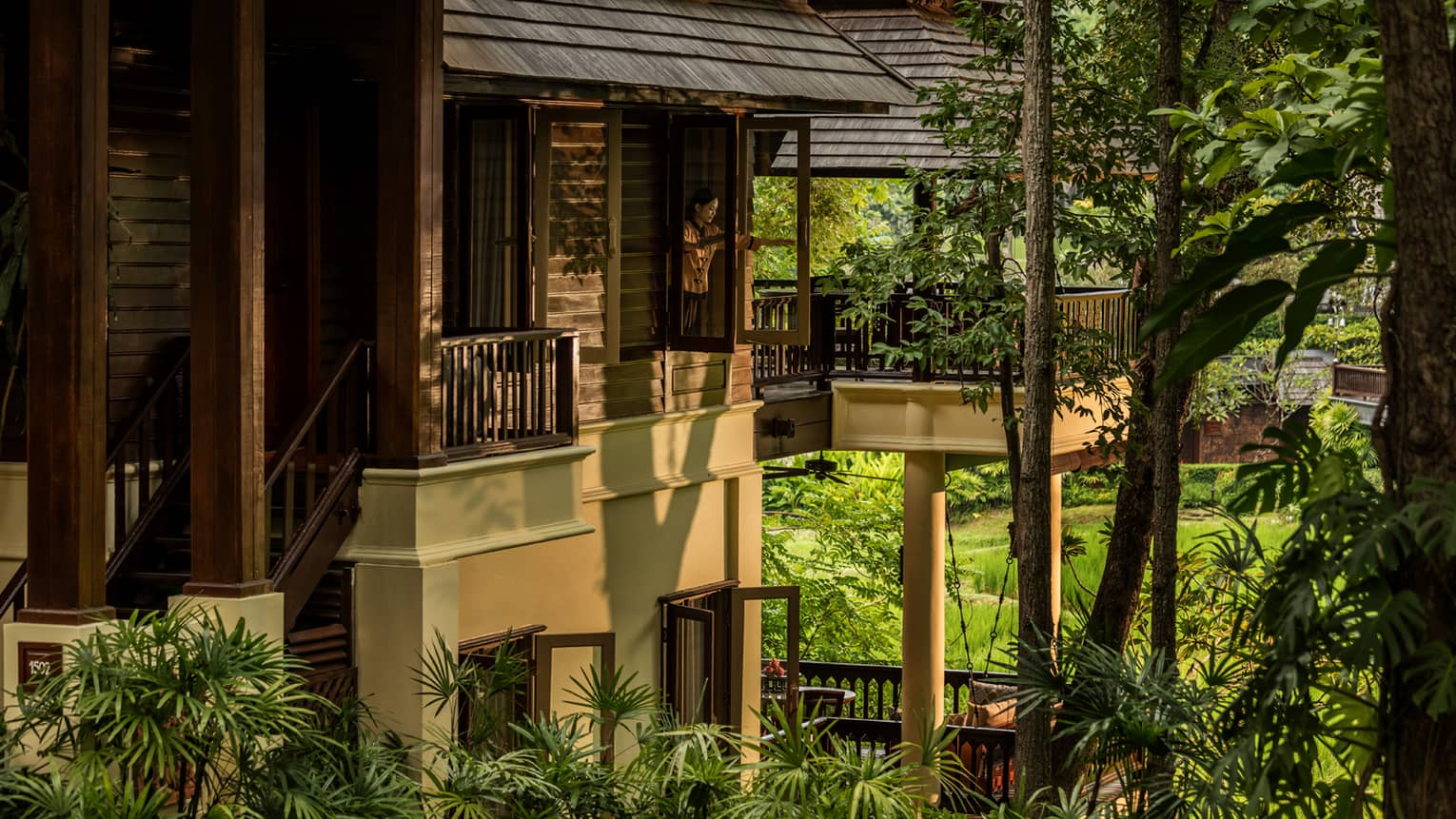 Person standing on balcony surrounded by lush greenery