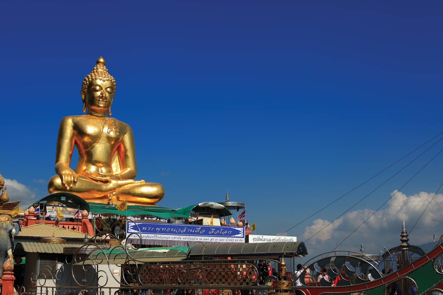 Gold Buddha statue on temple roof against a blue sky