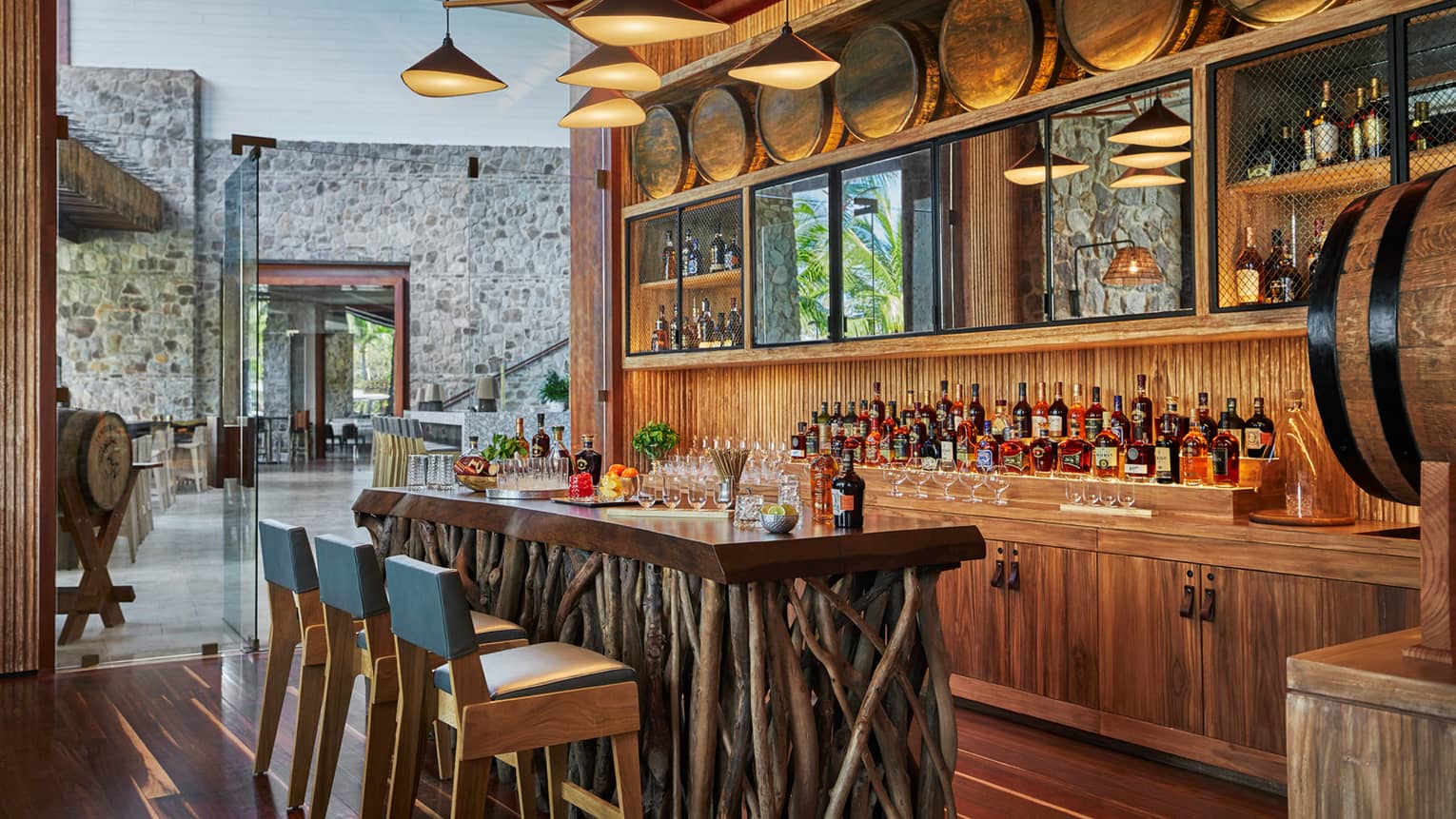 Modern chandelier above rustic wood tasting bar made from sticks, blue chairs, liquor display, barrel