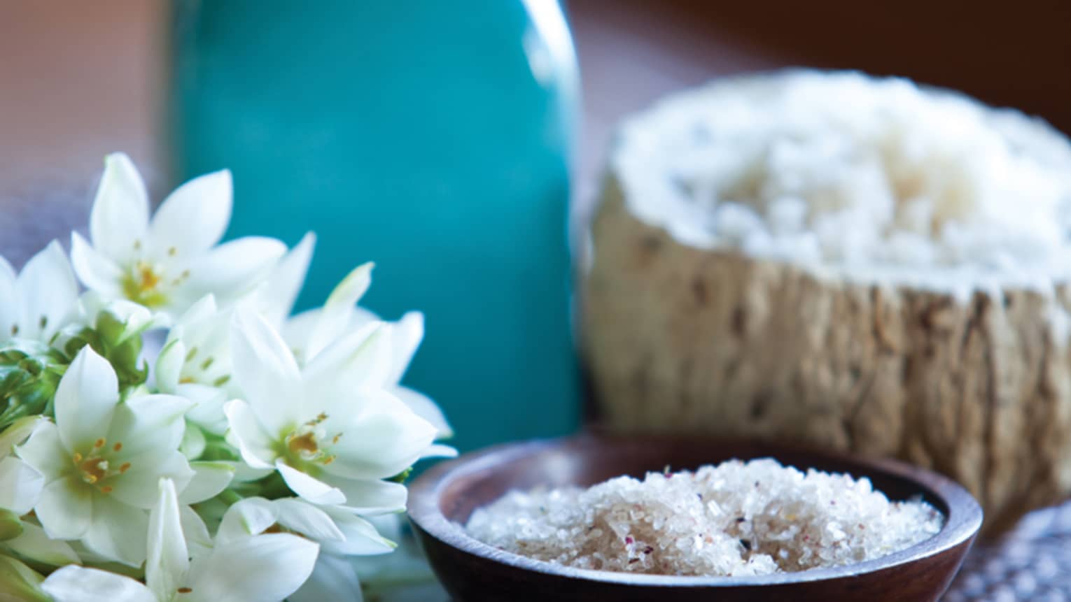 Brown wood spoon, bowl with spa salts next to fresh white flowers