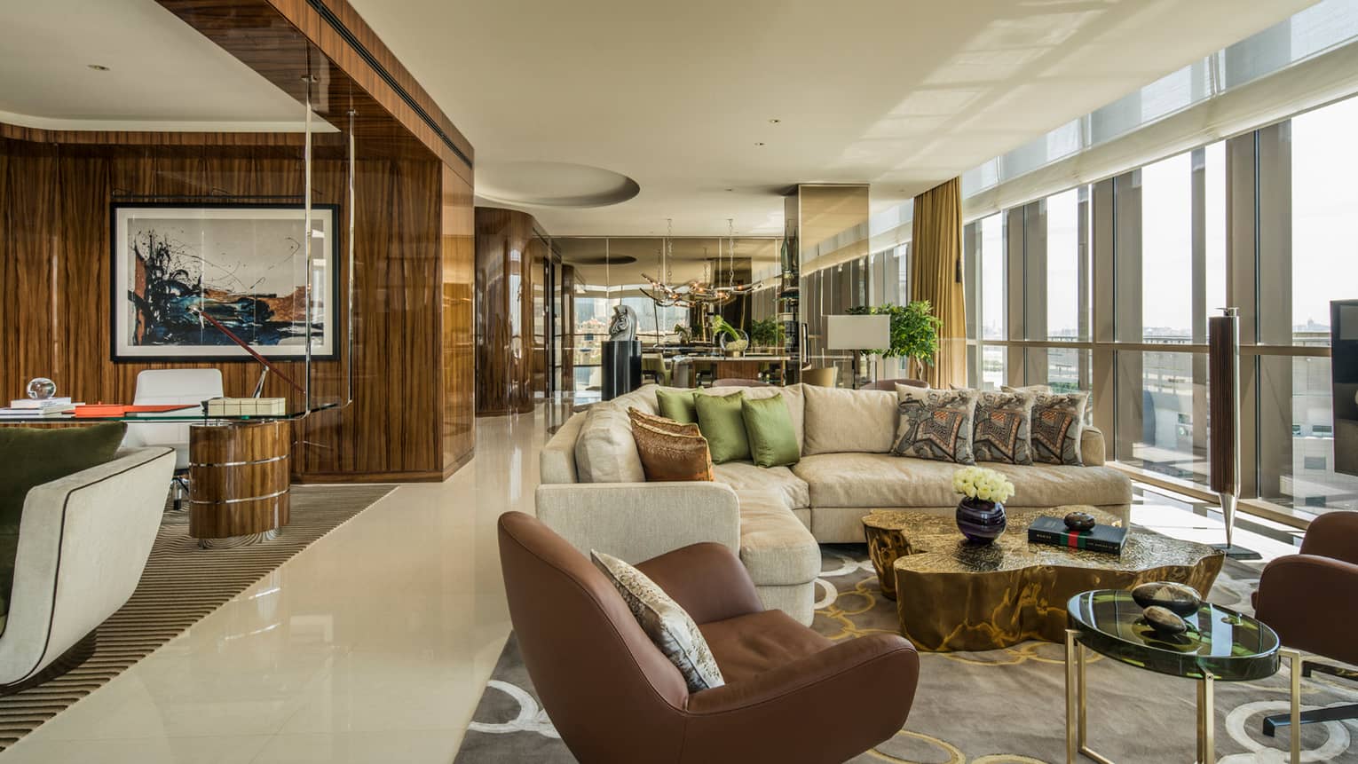 Penthouse Suite with large L-shaped beige sofa with pillows, leather armchairs, floor-to-ceiling windows along wall
