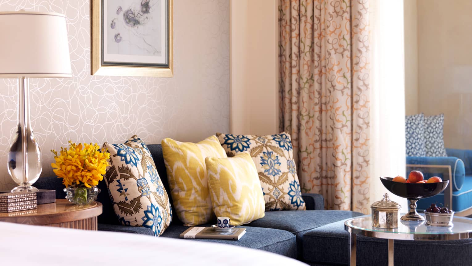 Close-up of blue sofa with yellow, blue and white pillows, book with small teacup resting on cushion