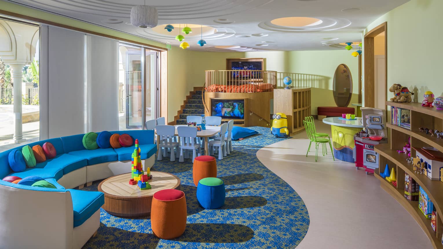 Complimentary kids centre room with curved, bright sofa and cushions, toys and TV loft