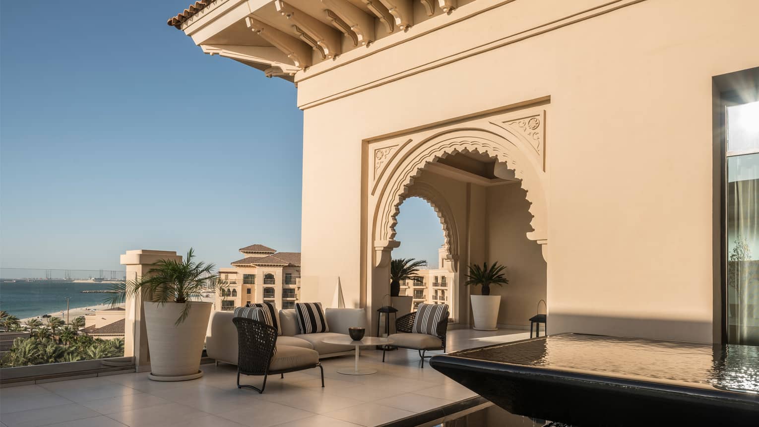 Large rooftop patio with villa-style exterior, white patio sofa, large tropical plants, overlooking beach