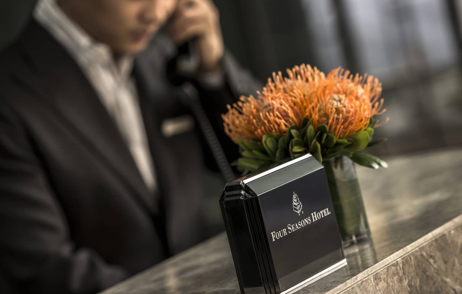 Close-up of Four Seasons Hotel concierge desk, orange flowers in vase, staff on phone