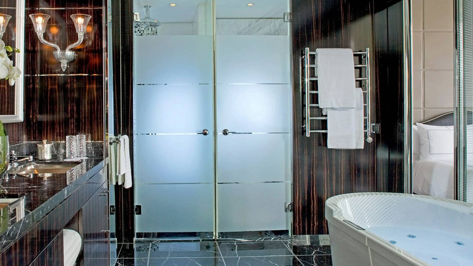 Presidential suite bathroom featuring dark marble accents, a frosted glass door, a towel warmer and a modern bathtub 