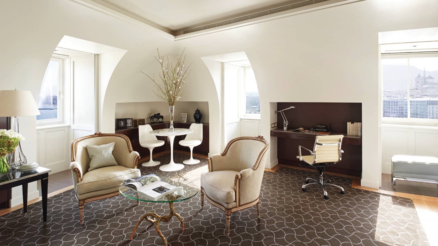 Four Seasons executive suite with antique-style armchairs, a glass coffee table, modern dining set, built-in desk and arched windows offering city views