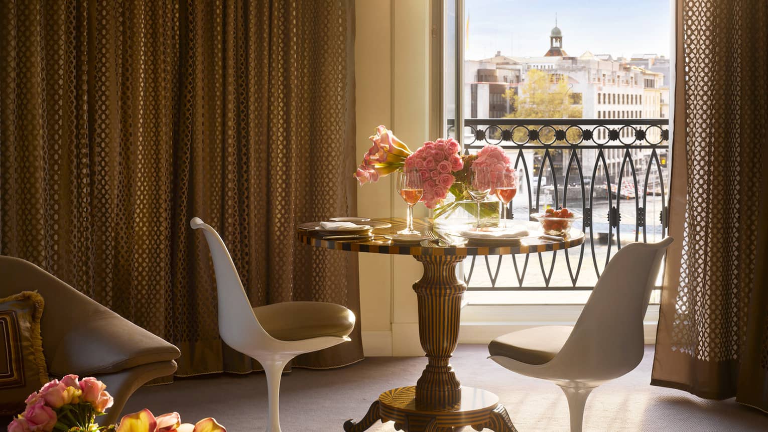 Luxury hotel elegant dining area with a small round table set with wine and flowers by a balcony overlooking the city
