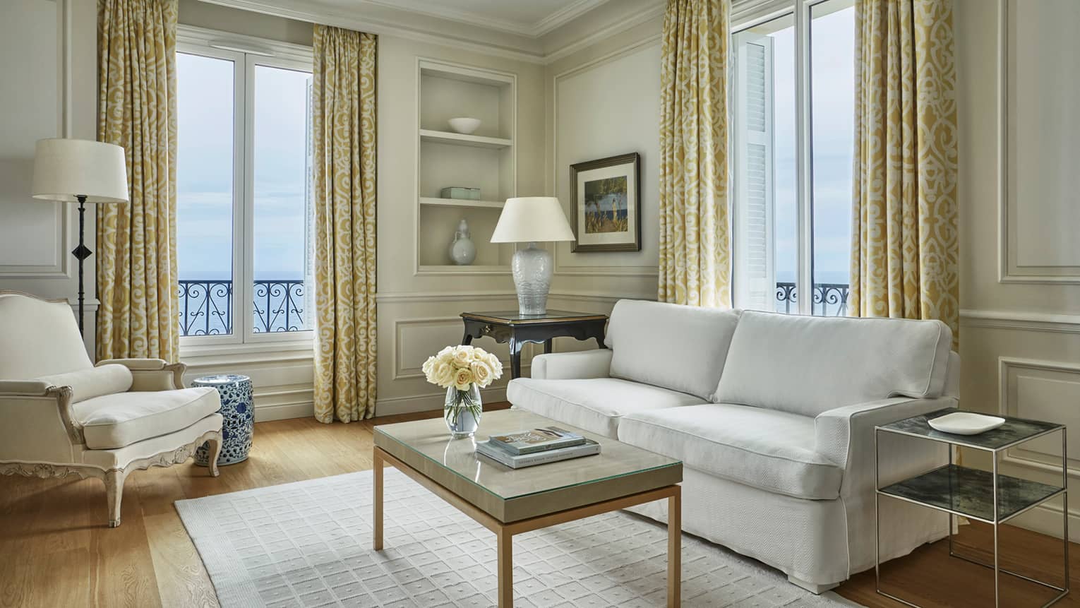 Modern white sofa, armchair, rug, table with books, flowers, corner windows