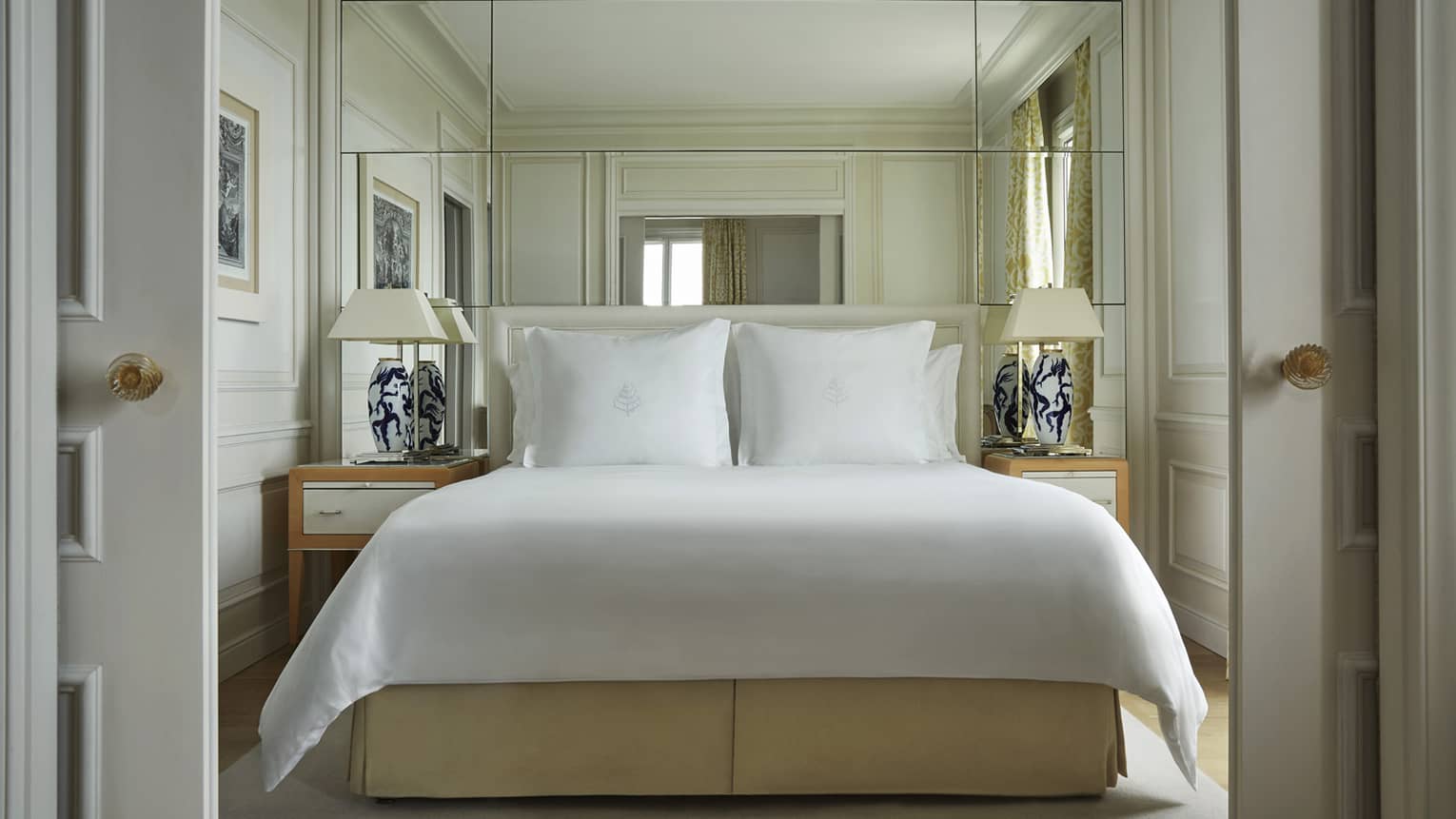 Modern white hotel room with bed flanked by lamps and against mirrored wall