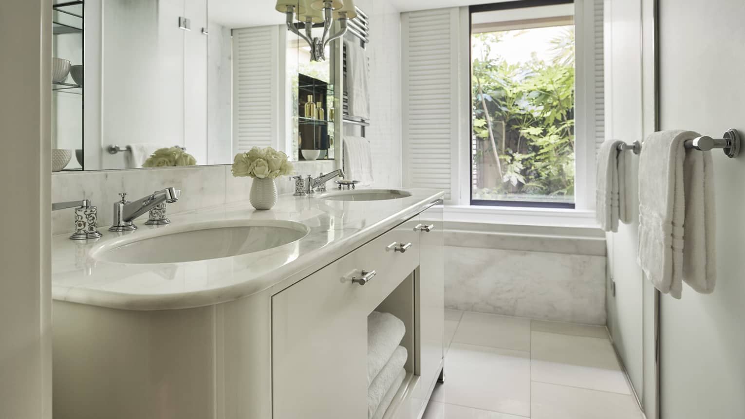 Hotel room full-marble bathroom with double vanity, plate mirror and view of greenery outside window over soaking tub