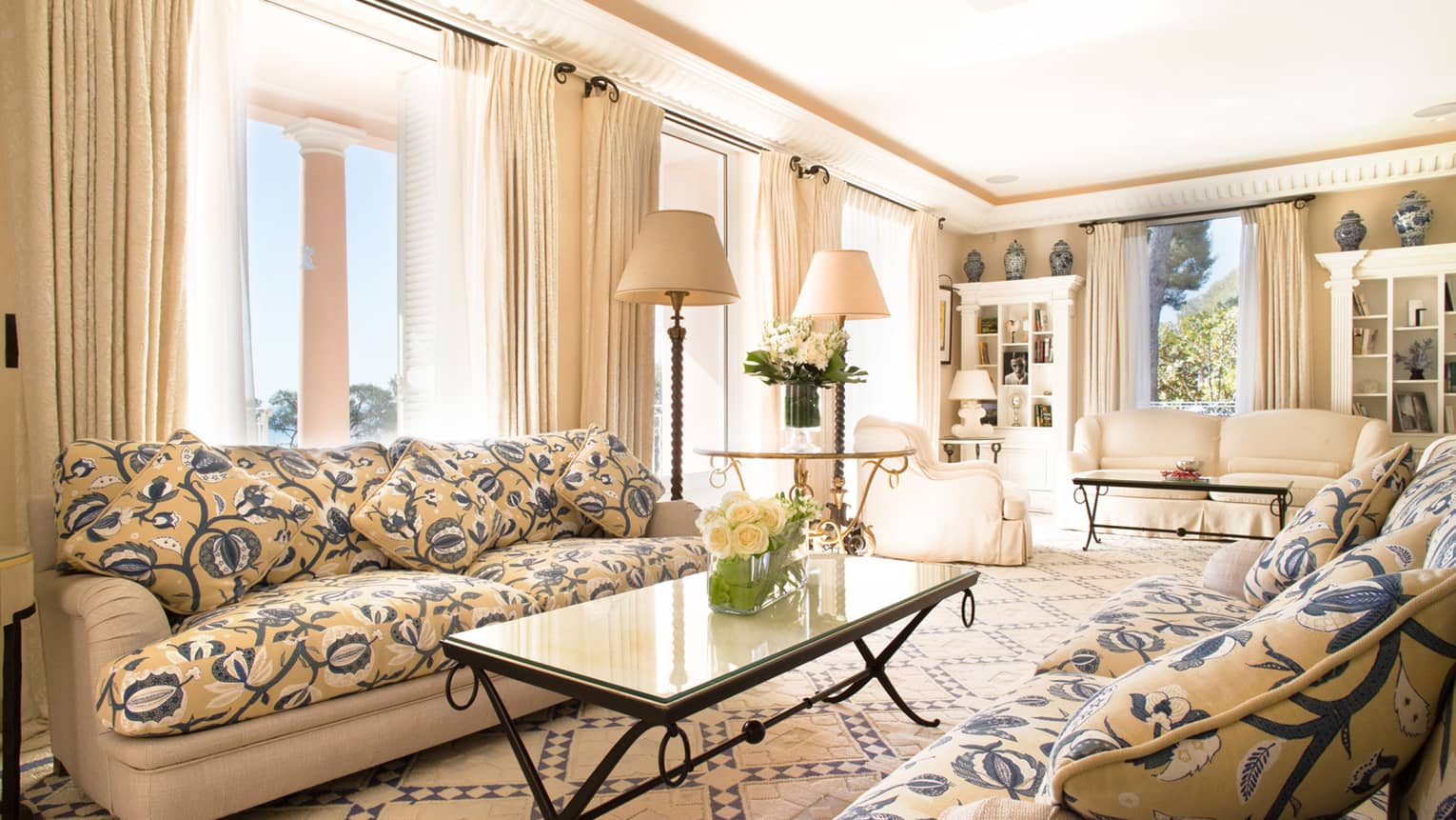 Floral sofa, coffee table with white roses in bright living room with cream armchairs, drapes