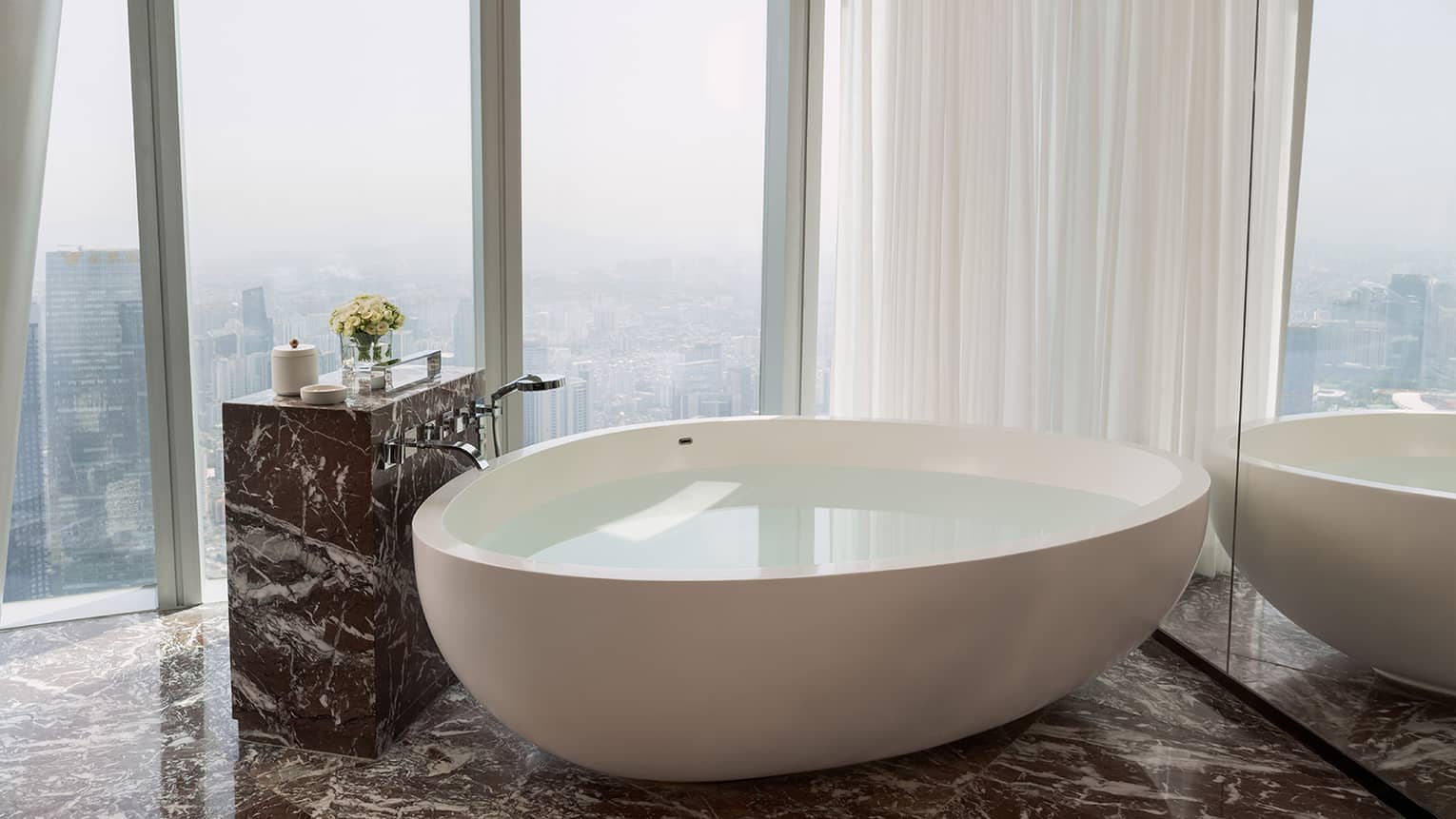 Bathroom with wall of windows overlooking city, and a large free-standing tub next to the windows