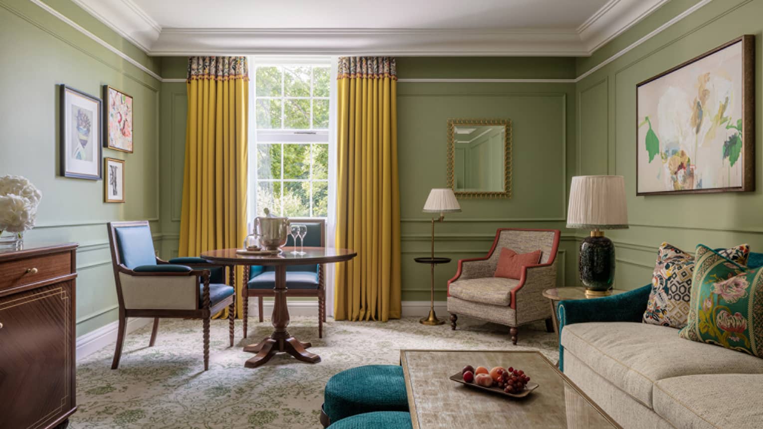 Guest room with cream couch and matching accent chair, coffee table, small round table for two, avocado-coloured walls, window with yellow drapes