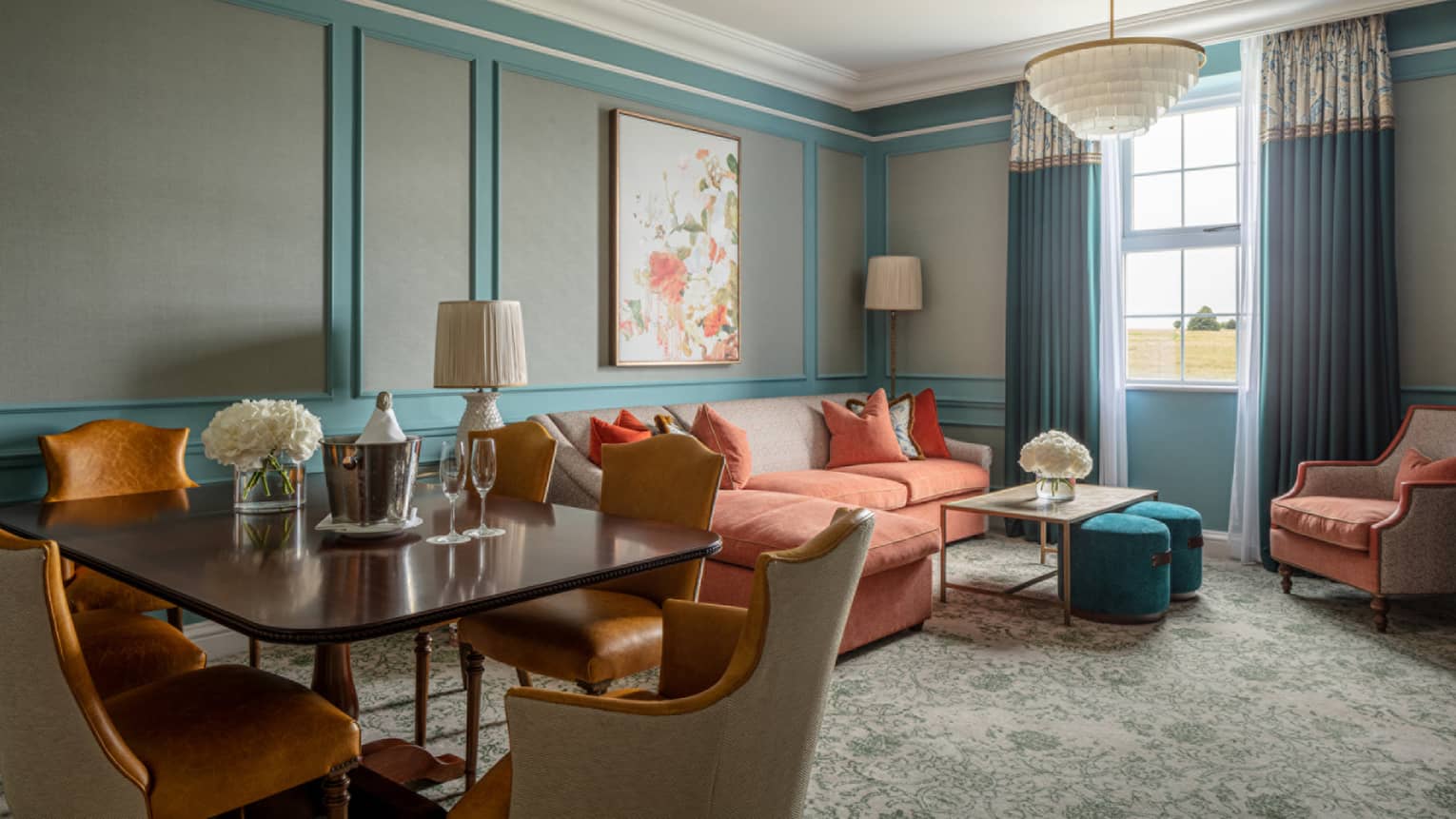 Guest room lounge area with red sectional sofa, coffee table, accent chair, rectangular dining table with six chairs, paisley carpeting, window with blue drapes