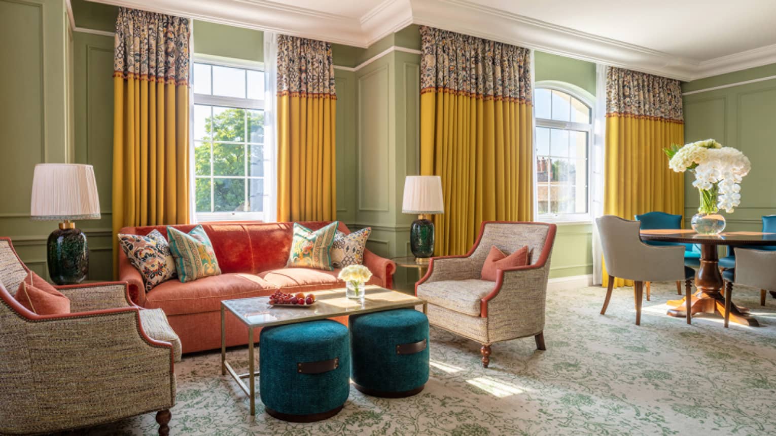 Guest room with red couch, two cream accent chairs and coffee table, dining table with four chairs, twin windows with yellow drapes
