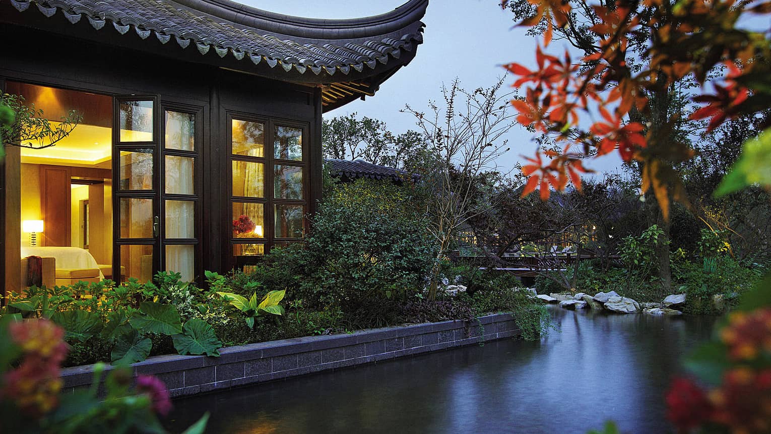 Side view of Lake Suite villa with sweeping roof, garden over water at night