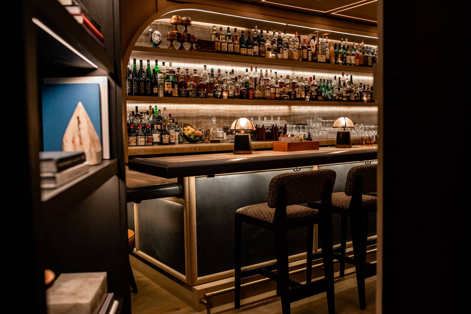 A bar with many bottles of liquor behind a bookcase.