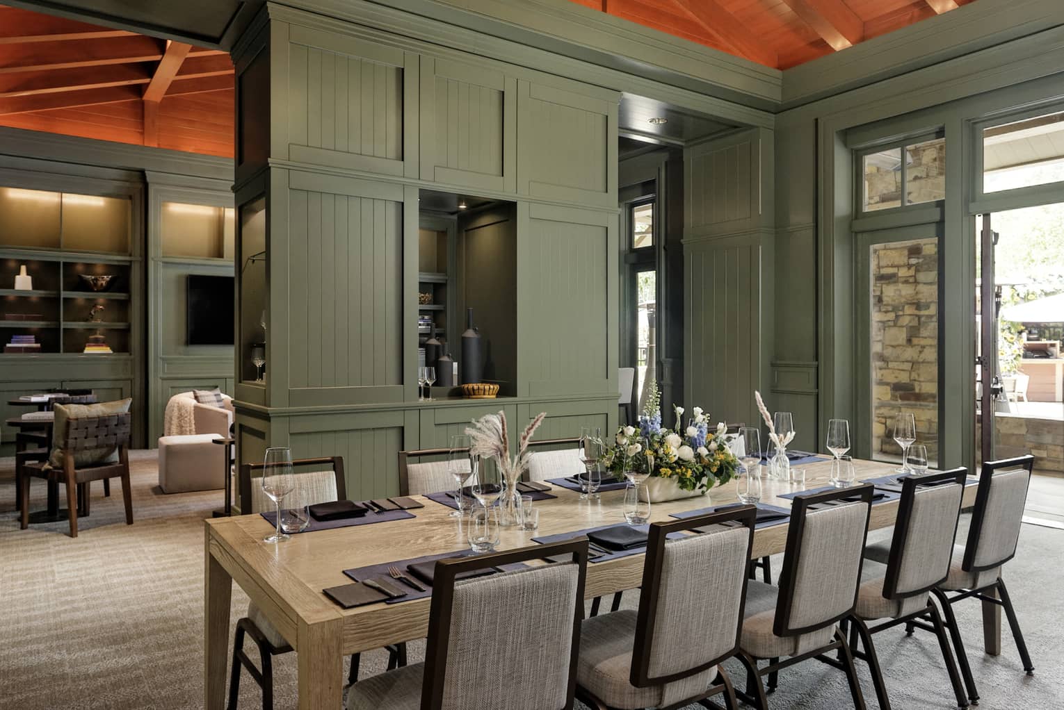 A dining room with green walls and a table set with flowers, glasses and place mats