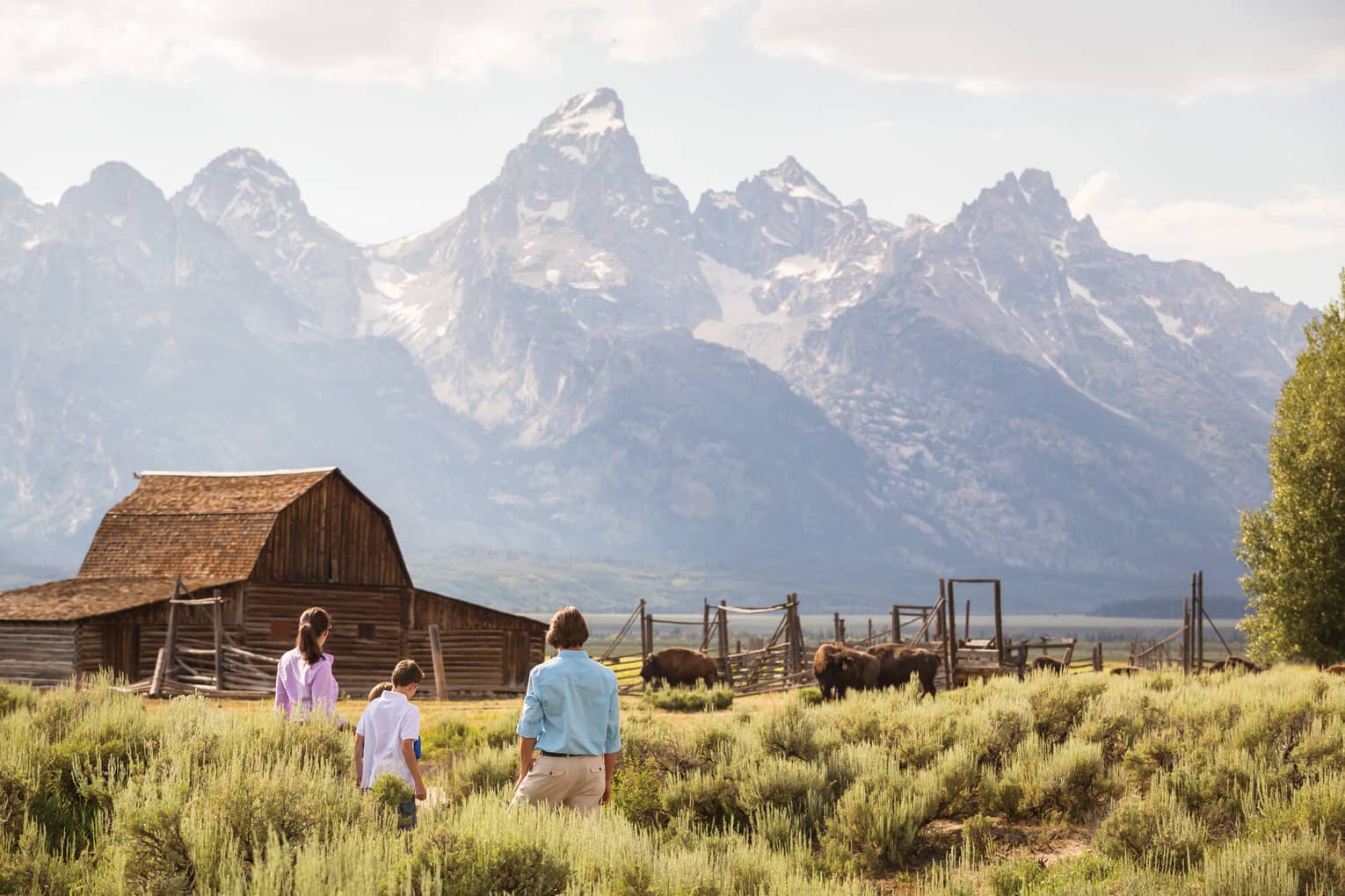 Family standing in a field with a cabin and mountains in the background.